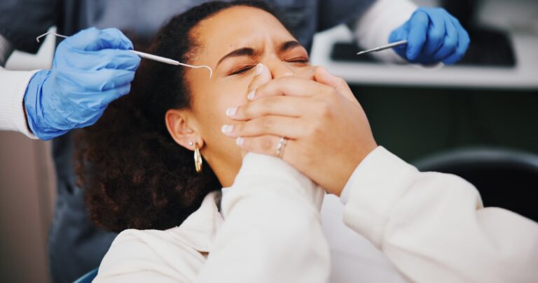 scared woman in a dental chair covering her mouth with both hands, dental anxiety